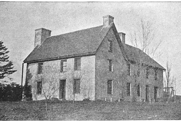 Photograph of a large stone house with multiple chimneys and small windows set on a grassy slope