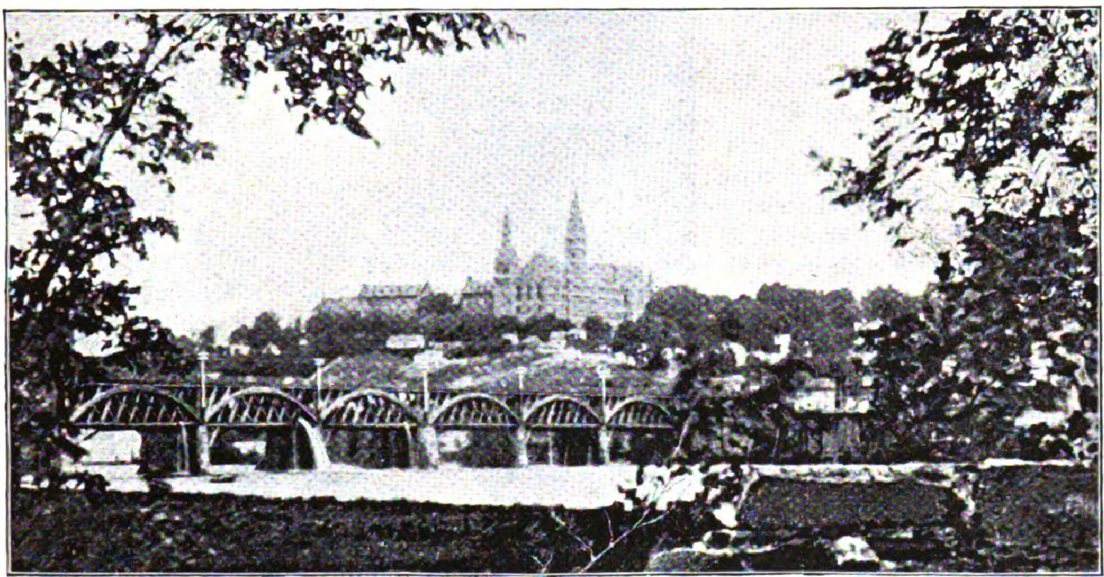 River view with arched bridge and distant buildings visible through trees