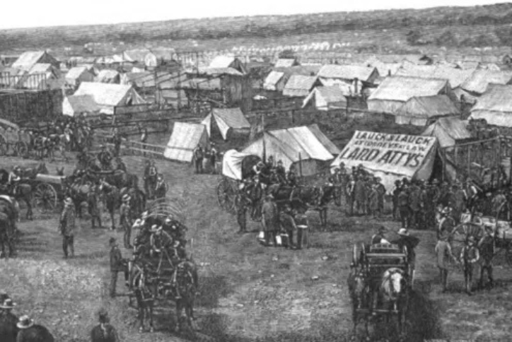 A view of Guthrie on April 27th showing the town site crowded with white tents, horse-drawn wagons, and the beginnings of wooden frame structures under construction.